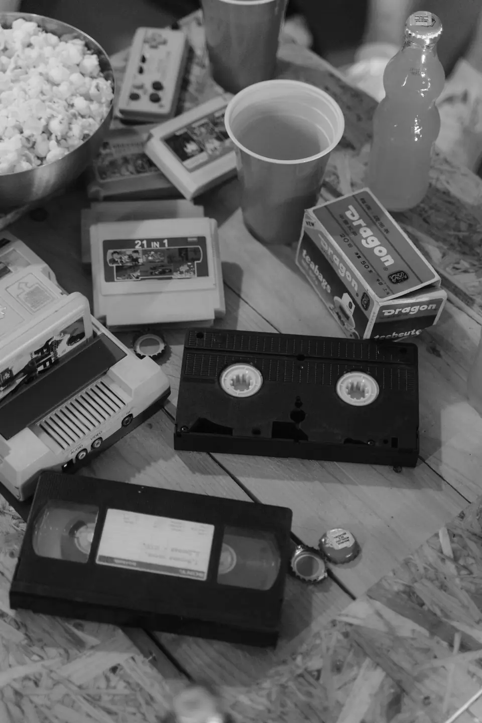 Videocassettes, game cartridges, a bowl of popcorn and drinks cover a wooden tabletop.