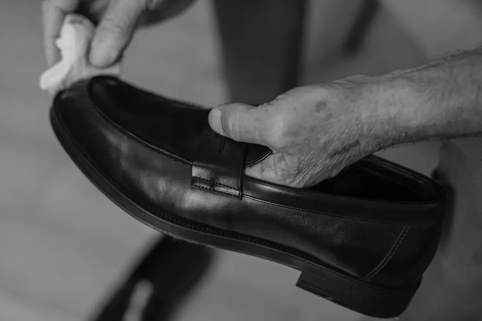 Two hands polish a dark leather loafer with a white cloth, one hand braced inside the shoe.