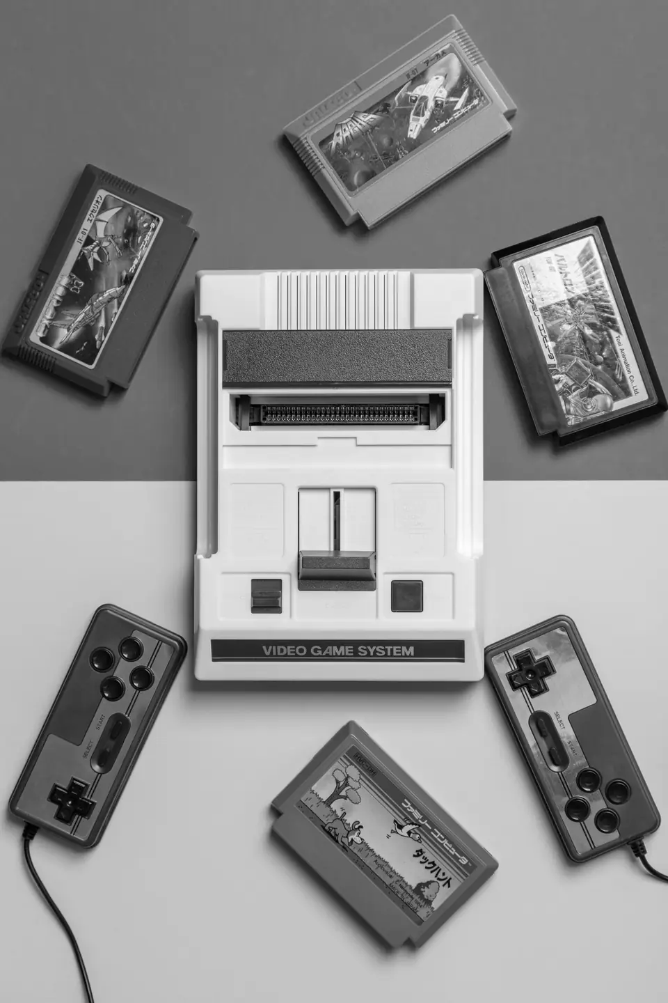 A white retro game console sits surrounded by four cartridges and two wired controllers.