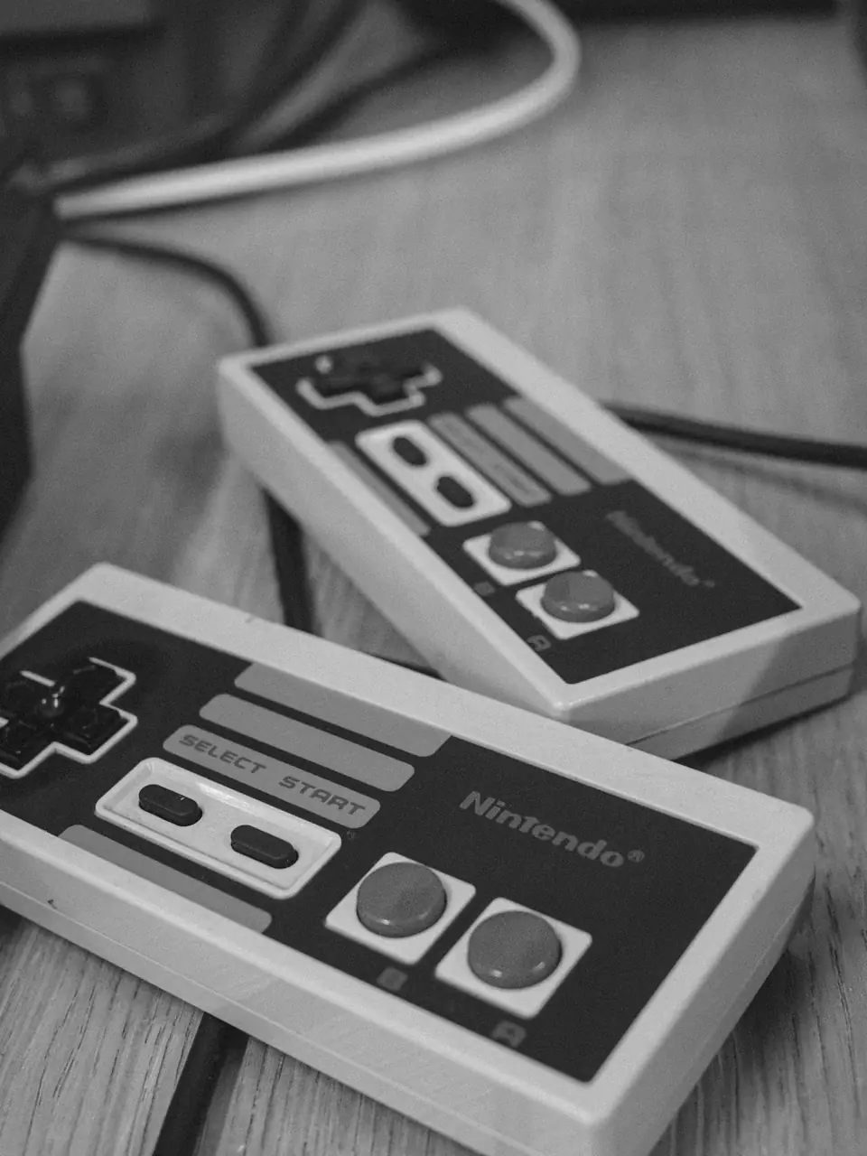 Two Nintendo game controllers with direction pads and red buttons lie on a wooden table.