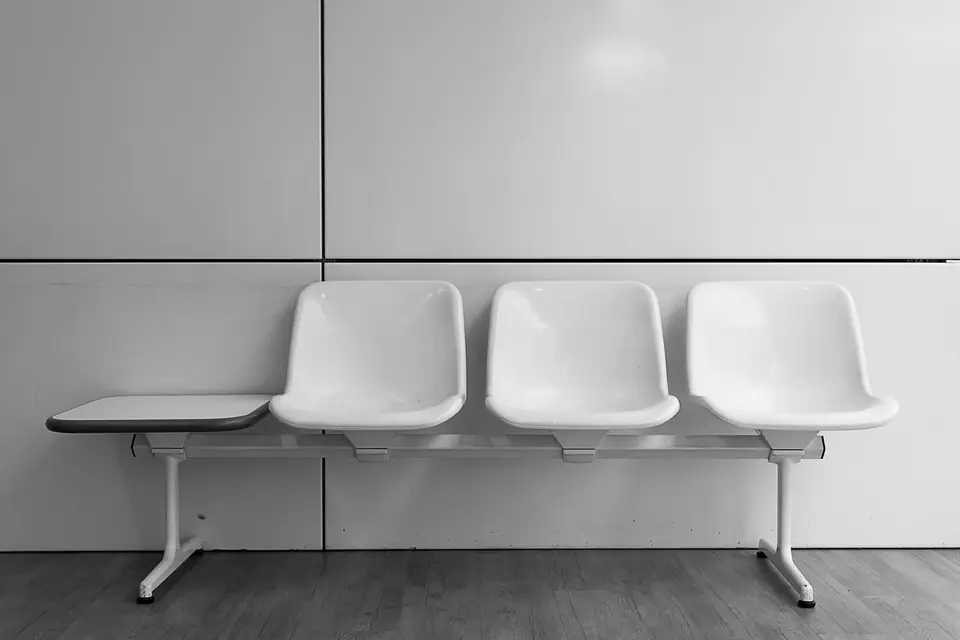 Three white plastic seats and a small side table on a metal frame against a plain wall.