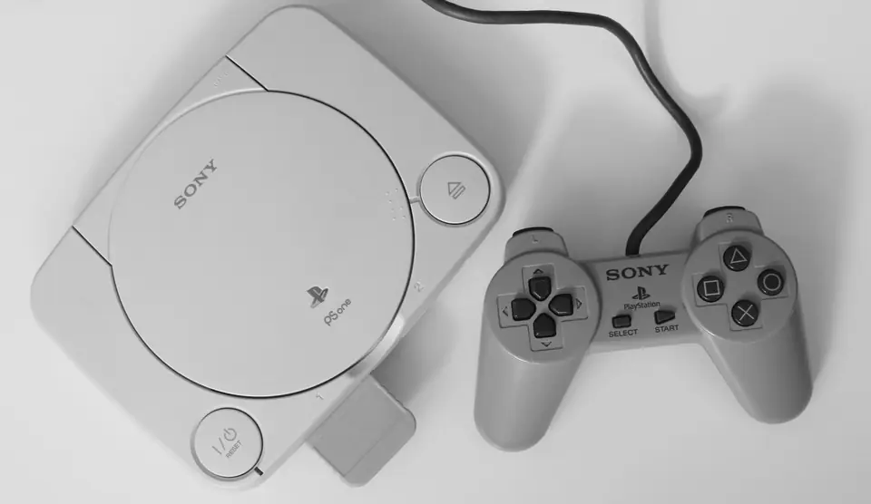 A small white game console with a round lid sits beside a gray wired controller.