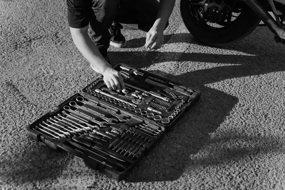 A person crouches beside a motorcycle and reaches into a large open tool case on the pavement.