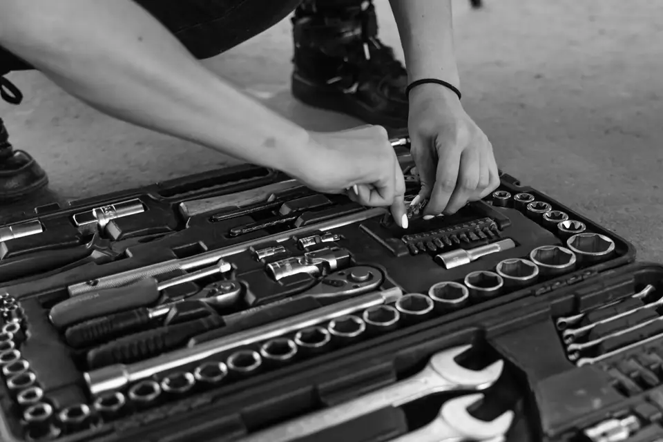 Hands select a piece from an open socket wrench set with rows of sockets and wrenches on a concrete floor.