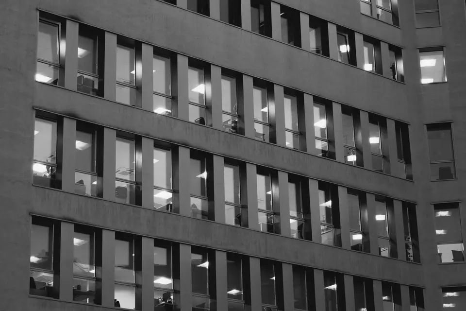 The facade of an office building with rows of windows, some of them lit from inside.